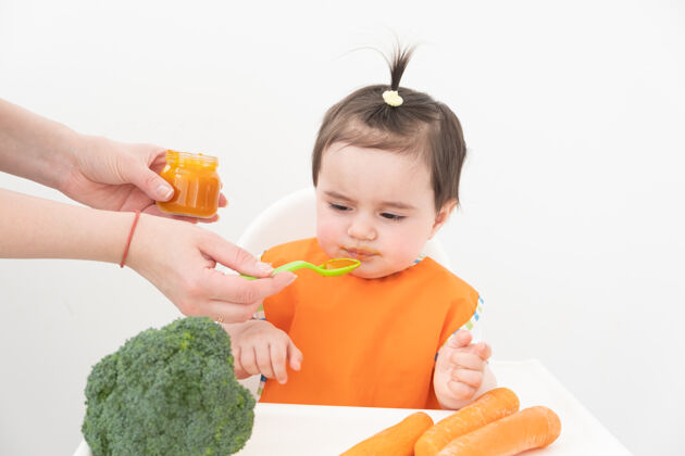 饮食坐在儿童椅上吃白色蔬菜泥的女婴背景妈妈喂宝宝胡萝卜母亲房子