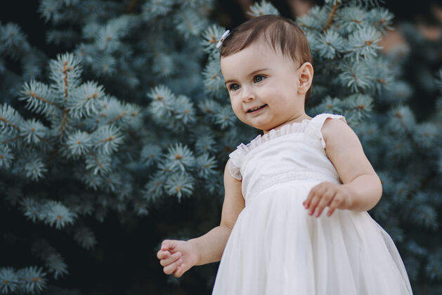 站站在松树前穿着白裙子的漂亮女婴表情公园小