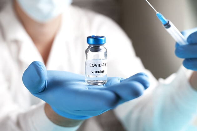瓶子研究人员手里拿着Covid-19疫苗 男医生穿着白大褂 戴着医用口罩 戴着蓝色手套 手里拿着装有治疗冠状病毒疫苗的注射器和瓶子冠状病毒治疗的概念治疗防护科学