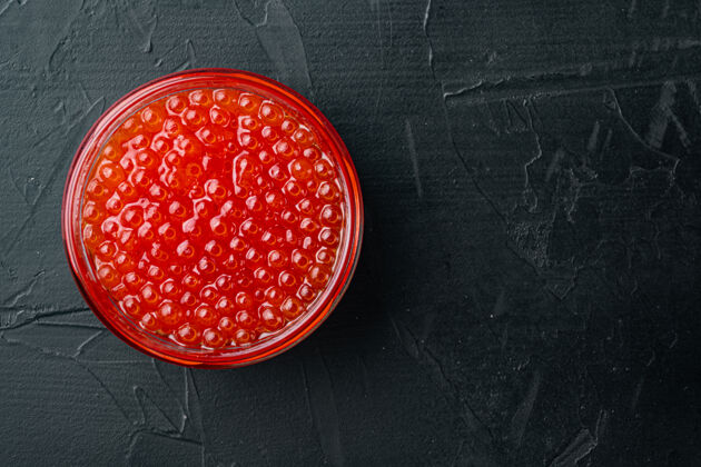 鳟鱼红色鱼子酱罐 放在黑色的桌子上 俯视平躺红鱼子酱玻璃罐子