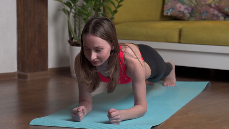 健康穿着运动服的漂亮年轻女子晚上在家里的瑜伽垫上做平板运动人力量活动