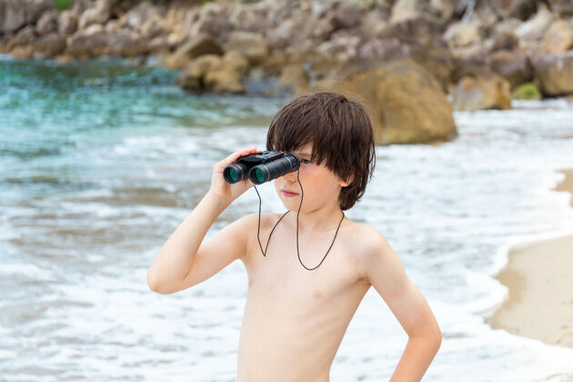 天空一个小男孩呆在海边的海滩上 用望远镜看东西手表童年青年