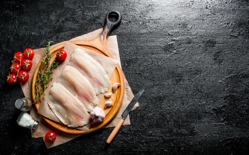 食物用刀把鱼片放在圆形的砧板上 百里香 西红柿和香料放在黑色的乡村桌子上乡村百里香膳食