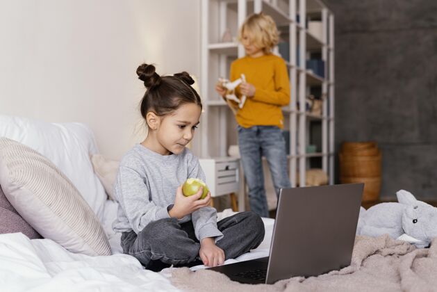 孩子兄弟姐妹在床上看笔记本电脑上的视频男孩苹果设备