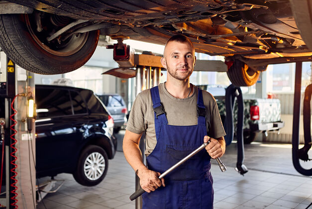 车间帅气的汽车修理工在加油站检查汽车的传动装置人扳手修理工