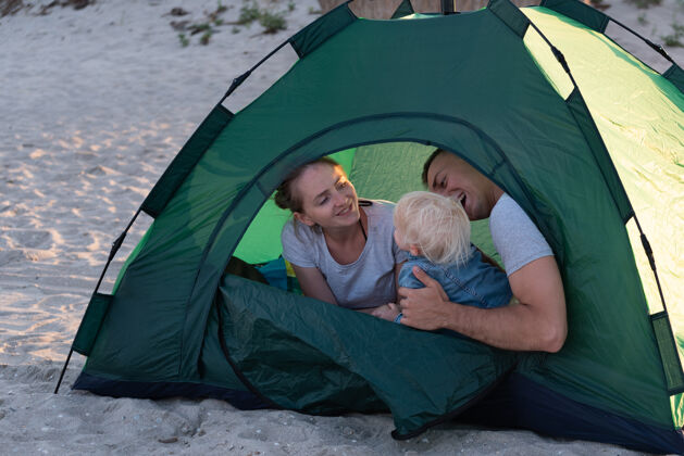 女孩一个年轻的家庭带着孩子在绿色的旅游帐篷里露营地.假期和孩子们在一起孩子儿子假日