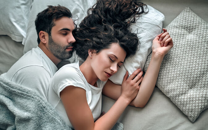 舒适俯瞰美丽的年轻夫妇拥抱而睡在一起 在家里的床上和平拥抱毯子