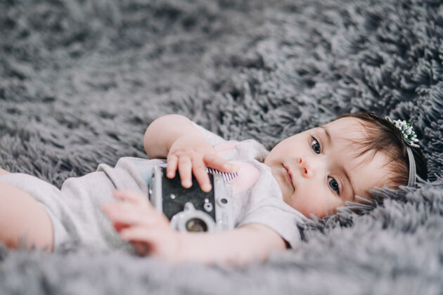 小可爱的婴儿抱着老式单反相机 躺在柔软的灰色床单上的特写镜头设备婴儿摄影