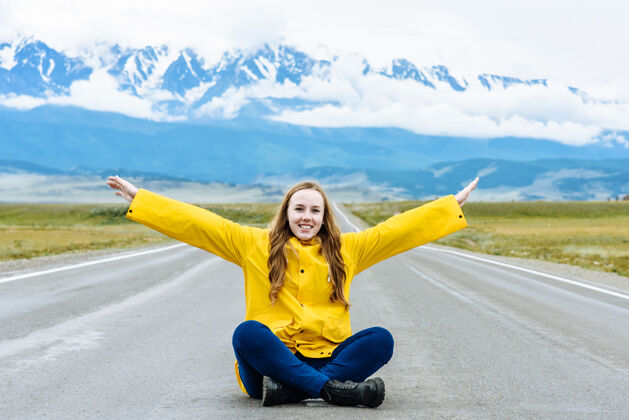 快乐一个年轻的快乐女孩徒步旅行者举着双手坐在山的背景下的山路上户外女人自然