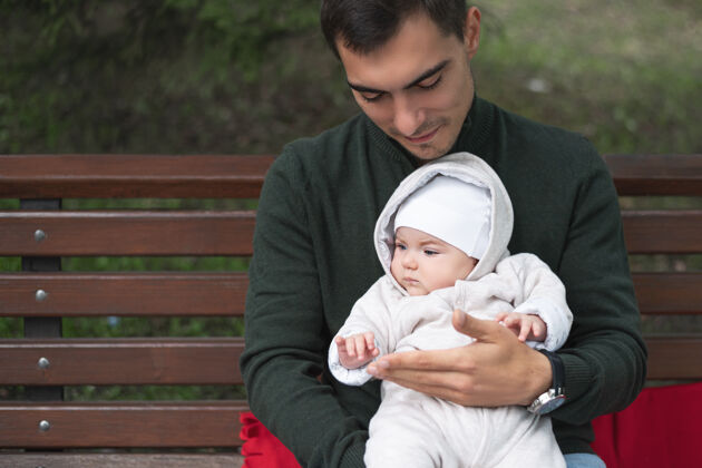 女婴特写单亲父亲坐在长凳上抱着孩子在公园里爱父母婴儿