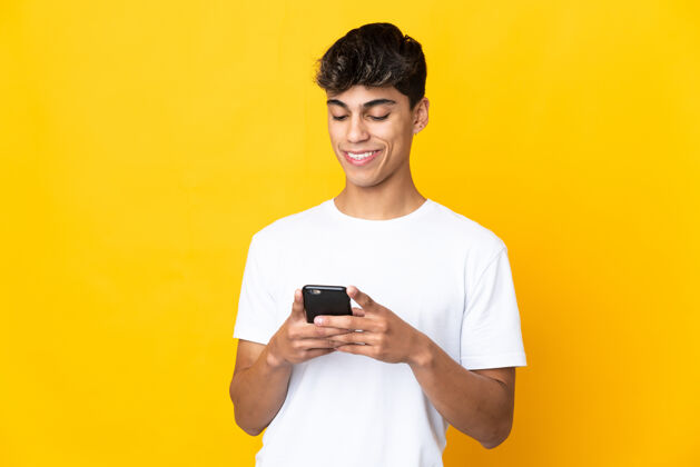 男人年轻人在孤立的黄色背景下用手机发送信息或电子邮件通讯好帅哥