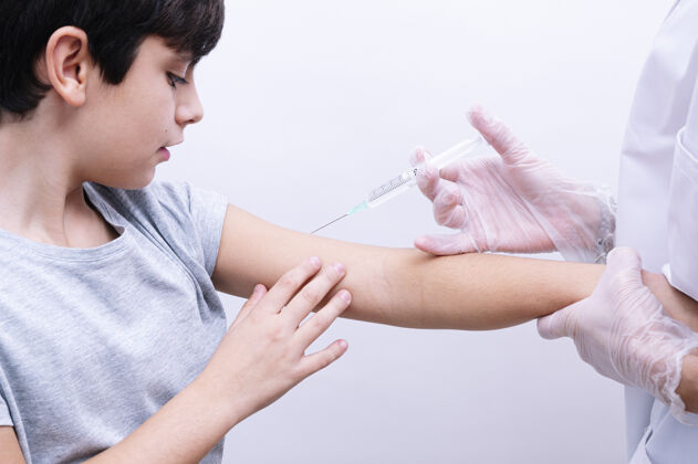 帮助一位戴着白色乳胶手套的护士在给卷发男孩注射疫苗的时候抓住他的肩膀注射孩子愈合