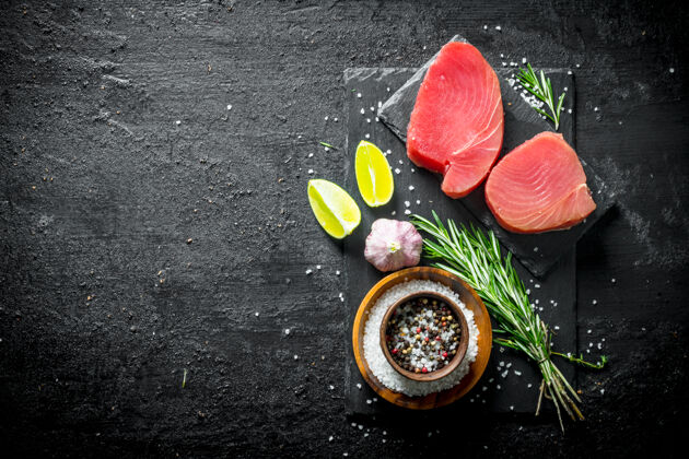日本一块新鲜的生金枪鱼放在石头板上 加上香料 大蒜 酸橙和迷迭香放在黑色的乡村餐桌上鱼食物有机