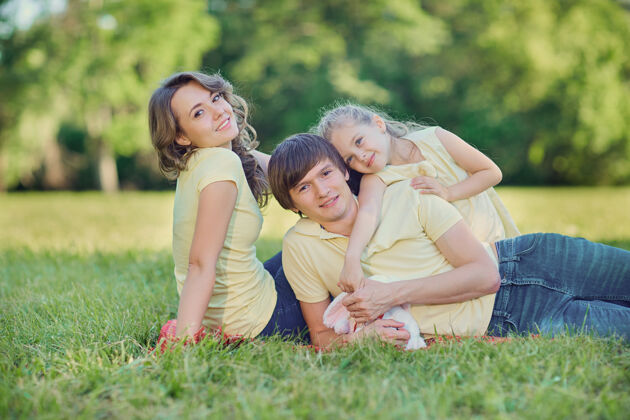 爸爸快乐的一家人躺在公园的草地上微笑拥抱女儿