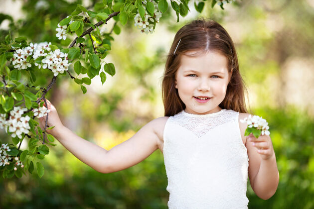 春天美丽微笑的小女孩穿着奶油色的裙子 映衬着夏日公园的绿色漂亮快乐开花