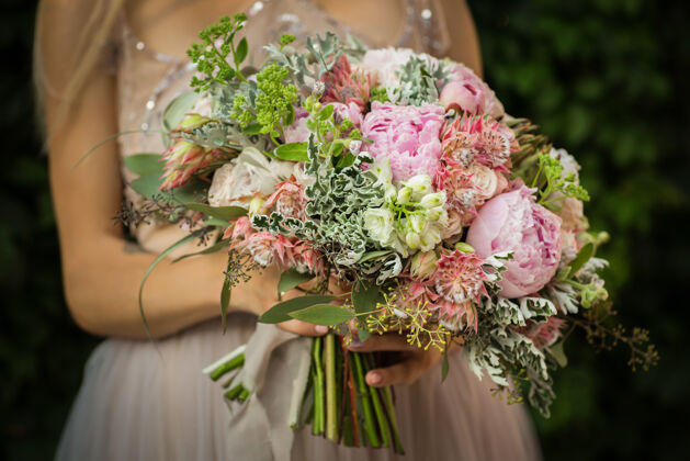 花束一位穿着灰色婚纱的优雅的 无法辨认的漂亮女人的肖像 在花园里摆姿势街头新娘捧着一束柔和的鲜花和绿叶婚礼户外订婚