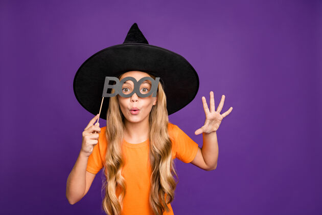 主题小巫婆扮演女巫角色万圣节派对手持纸棒恐怖造型穿橙色t恤巫师帽孤立紫色背景幽灵学前学校