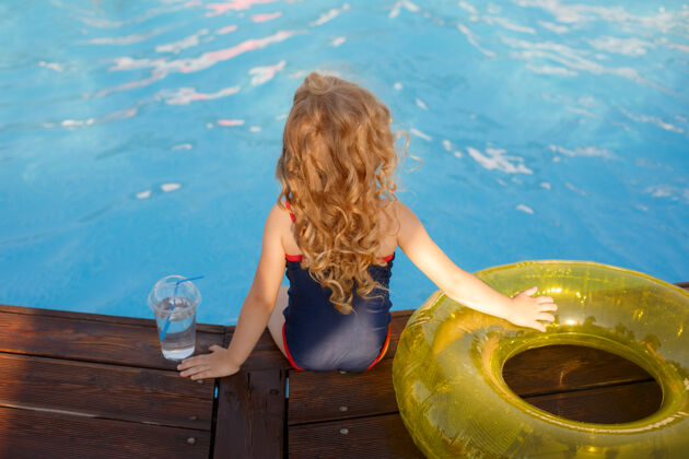 可爱戴着墨镜和泳装的小女孩 夏天坐在游泳池边热带放松欢呼