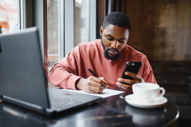 无线非洲年轻网店经理的个人资料照片 用手机与客户交谈工作人桌子