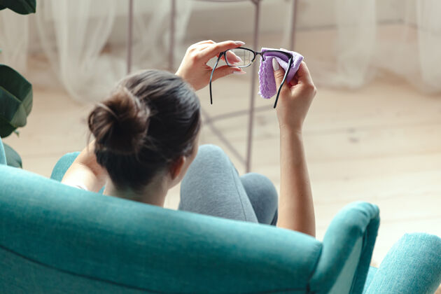 护理坐在沙发上用餐巾擦眼镜的年轻女子清洁抛光眼镜