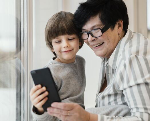 水平笑笑孙子和奶奶一起看智能手机设备祖父母女人