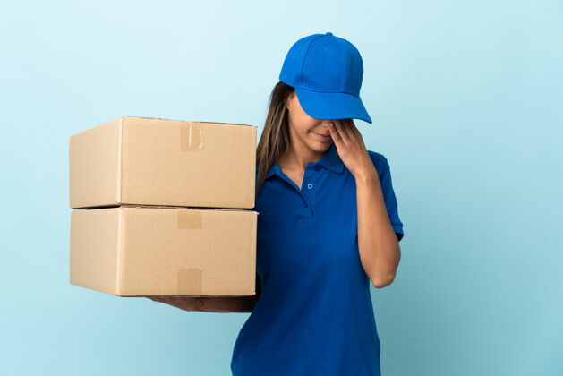 持有年轻的女送货员被隔离在蓝色的墙上 带着疲惫和病态的表情邮政问题负责人