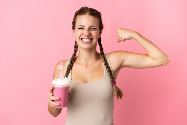 饮料年轻女子用草莓奶昔隔离在粉红色背景上做着强烈的手势女性积极胜利