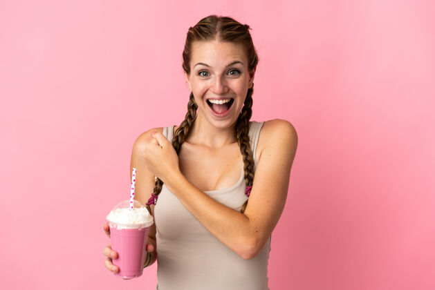 杯子年轻女子用草莓奶昔隔离在粉红色背景庆祝胜利水果欢乐欢呼