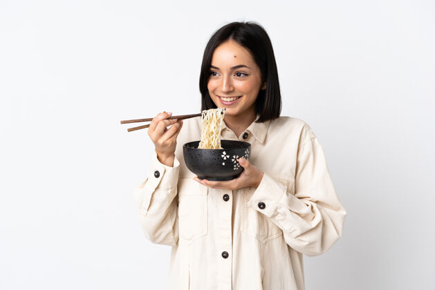 拉面一个年轻的白种女人被隔离在白墙上 用筷子端着一碗面条人位置五颜六色