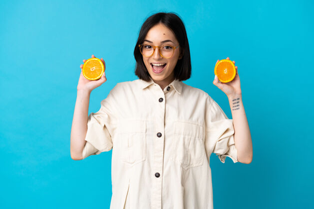快乐一个年轻的白人妇女拿着橘子被隔离在蓝色的墙上水果大笑食物