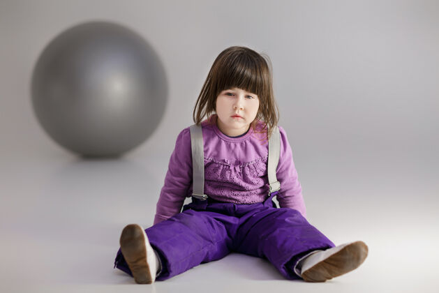 运动穿着紫色衣服的可爱小女孩 灰色背景上有一个健身用的大球背景可爱年轻