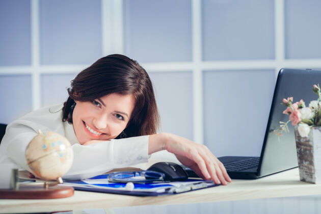可爱晚上坐在办公桌前的一个面带微笑的疲倦女人笔记本电脑无聊女性