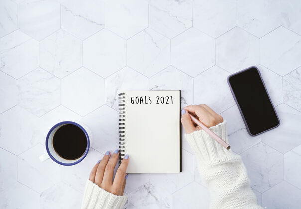 生活方式2021年的目标：女性在笔记本上写字 喝热咖啡 在白色大理石背景上使用智能手机 并提供复印空间 新年决心的概念食物圣诞节手