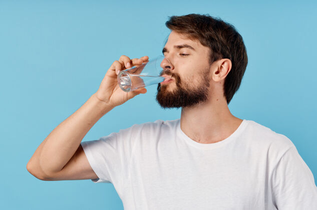 饮食在一张蓝色特写照片上 一个喝着杯子里的水的漂亮男人矿物人类口渴