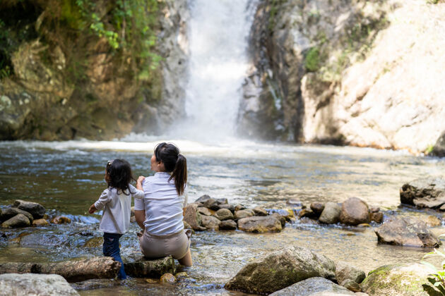在一起可爱的小女孩和妈妈坐在瀑布边自然女孩在一起