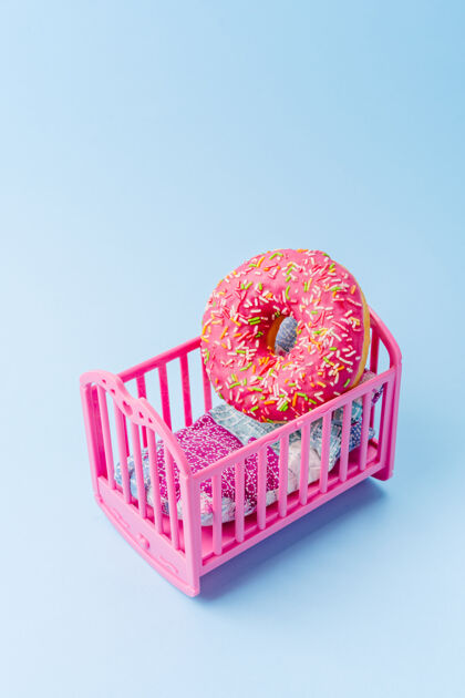 甜甜圈粉红色釉面上的甜甜圈 在一个带枕头和毯子的玩具粉色婴儿床上撒上五颜六色的小花圆形顶部小吃
