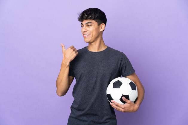 球年轻的足球运动员男子越过孤立的紫色背景 指着旁边的产品介绍微笑表情球员