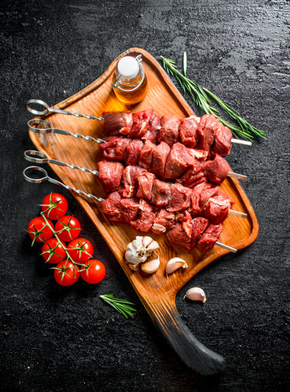 生的把生牛肉串放在砧板上 把西红柿 大蒜 迷迭香和油放在黑木桌上什什红色牛肉