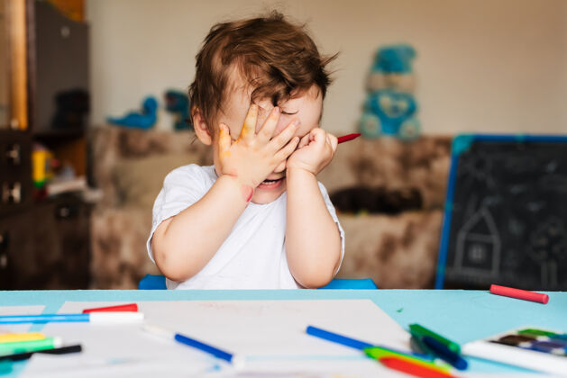 乐趣快乐的小男孩用彩色记号笔在一张纸上画画发展房子艺术