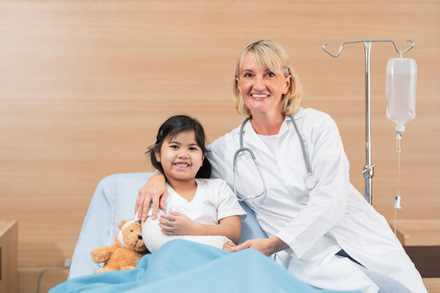 医学小医生儿科医生和小女孩病人随身带着泰迪熊在床上妇女健康听诊器