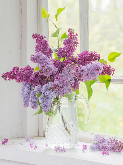 花一束紫丁香放在旧白色窗台上的玻璃罐里绿色背景花束
