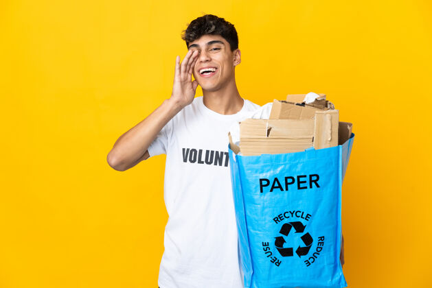 垃圾一名男子拿着一个装满废纸的回收袋 在孤立的黄色背景上大声喊叫 张大嘴巴谈话垃圾再利用