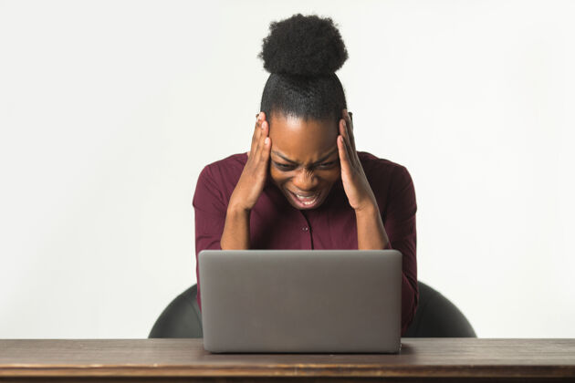 工作美丽的非洲年轻女子 笔记本电脑背景为白色表情悲伤互联网
