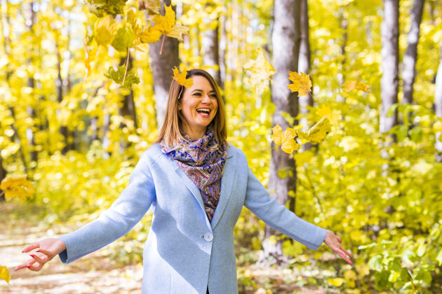 表情年轻有趣的女人在秋天公园扔树叶欢笑看起来女性