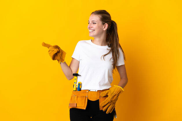 快乐被隔离在黄色背景上的年轻电工女士用手指着侧面展示产品车间修理指向