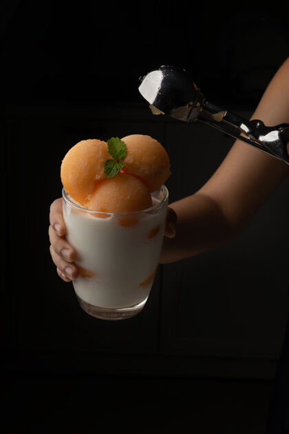 蜂蜜黄瓜瓜被舀成一个圆球状 像冰淇淋一样放进一个透明的杯子里 上面放着鲜奶 香甜可口好吃吃吧黑色背景上的照片哈密瓜饮食自然
