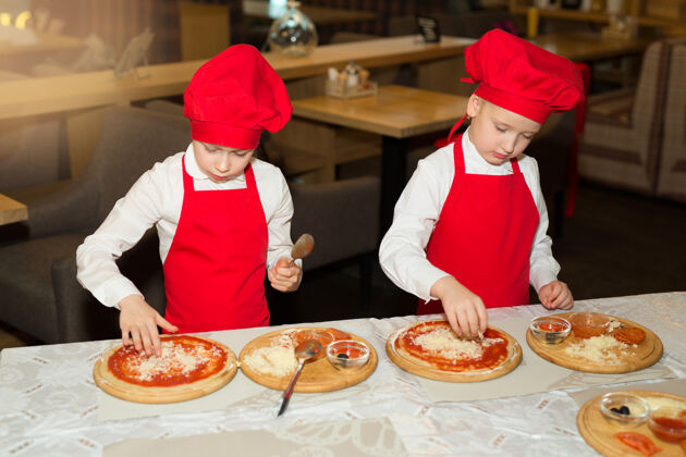 准备两个穿着白衬衫和红围裙的漂亮厨师女孩在餐厅做比萨饼朋友吃欢呼