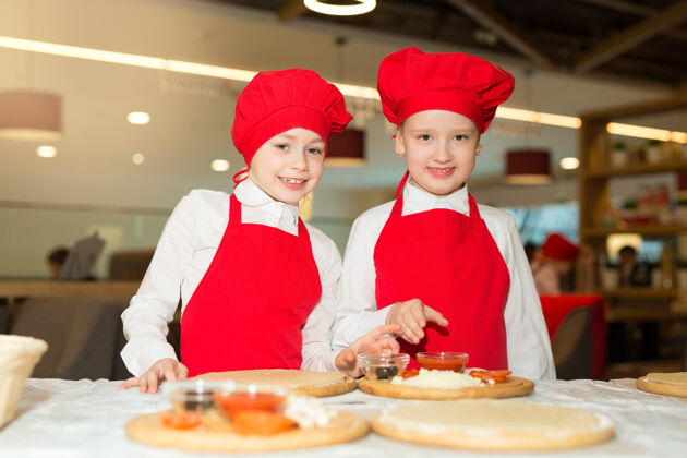 比萨饼两个穿着白衬衫和红围裙的漂亮厨师女孩在餐厅做比萨饼正面朋友专业