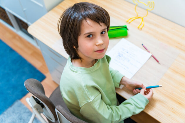 桌子小男孩坐在桌子旁做作业家集中儿童写作练习很高兴在家上学教育年轻书桌小学生