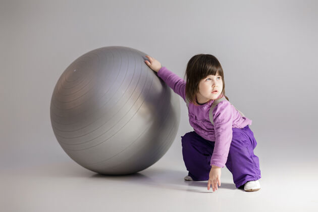 婴儿穿着紫色衣服的可爱小女孩 灰色背景上有一个健身用的大球玩耍小球
